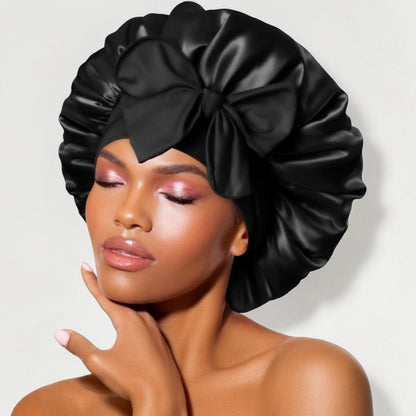 Black satin sleep bonnet with wide adjustable tie band and front bow, worn by woman