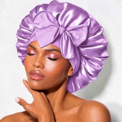Lavender satin sleep bonnet with wide adjustable tie band and front bow, worn by woman
