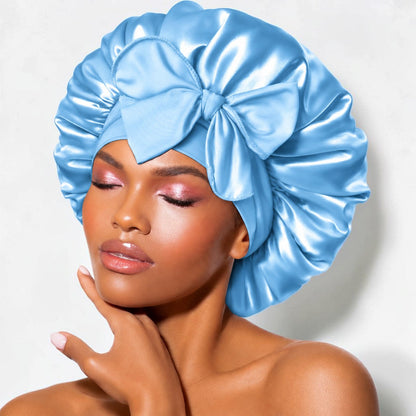 Light blue satin sleep bonnet with wide adjustable tie band and front bow, worn by woman