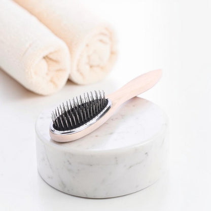 Wooden hair extension detangling brush with metal bristles on a bright white studio background