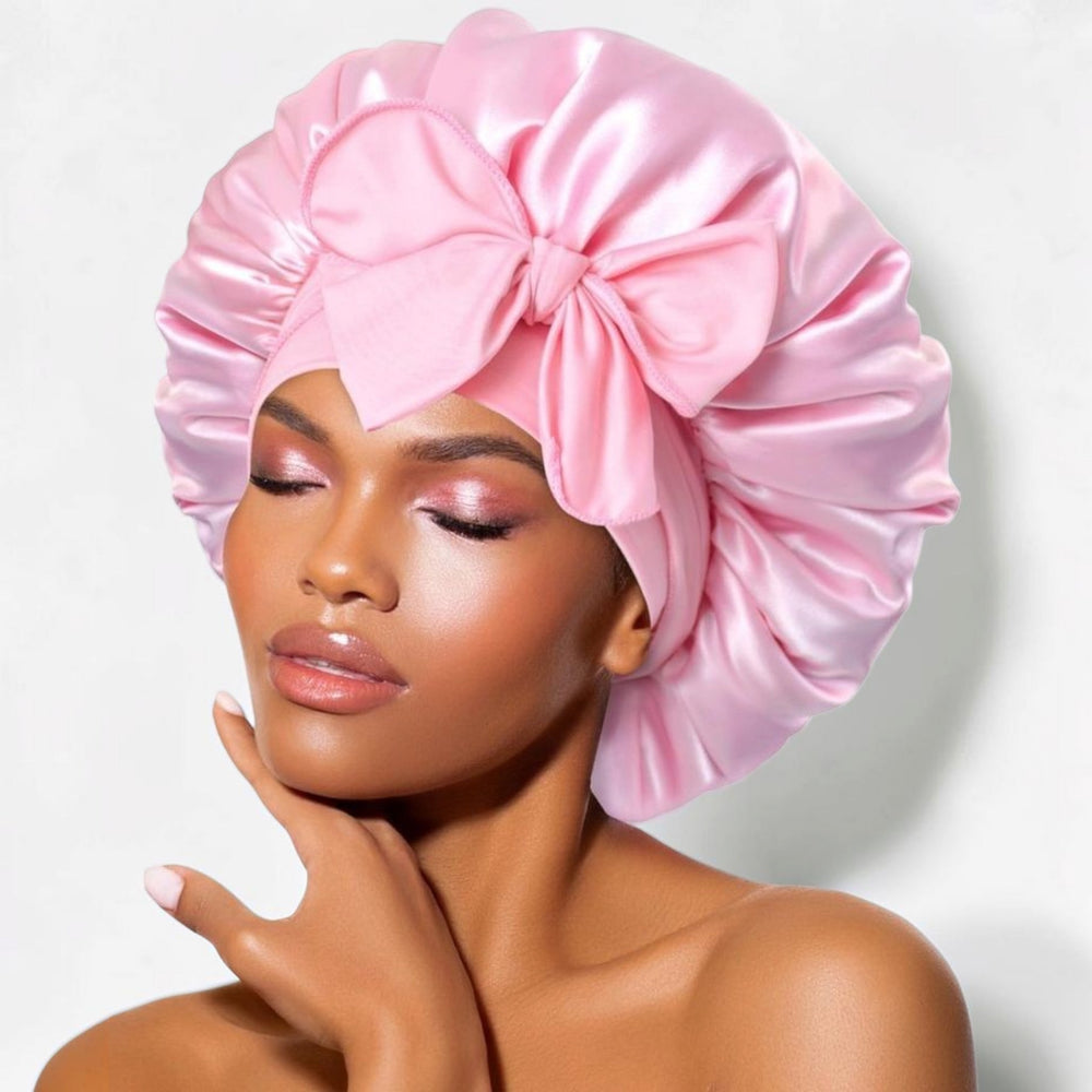 Pink satin sleep bonnet with wide adjustable tie band and front bow, worn by woman